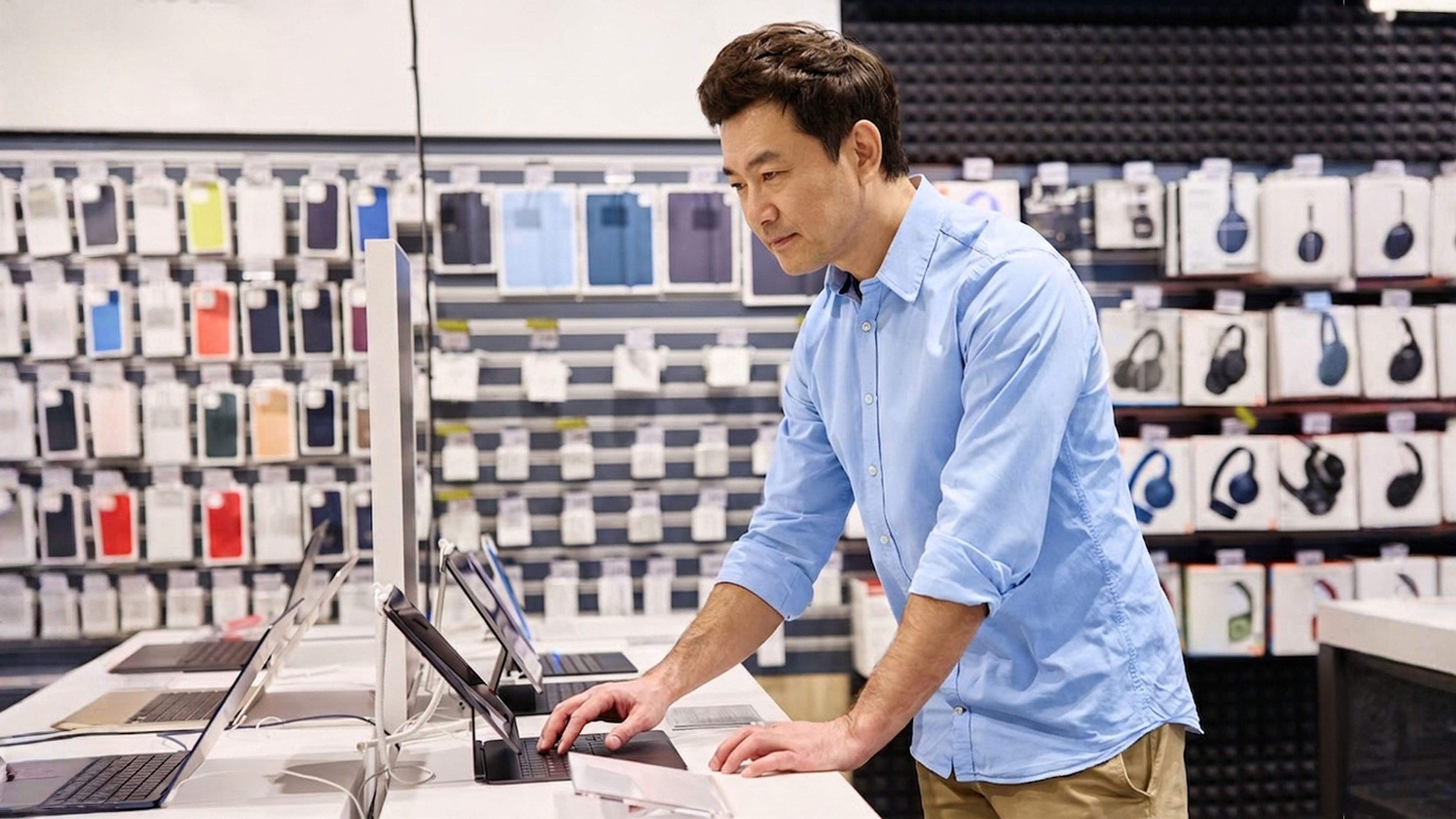 An asian man browsing over tablets in tech store.