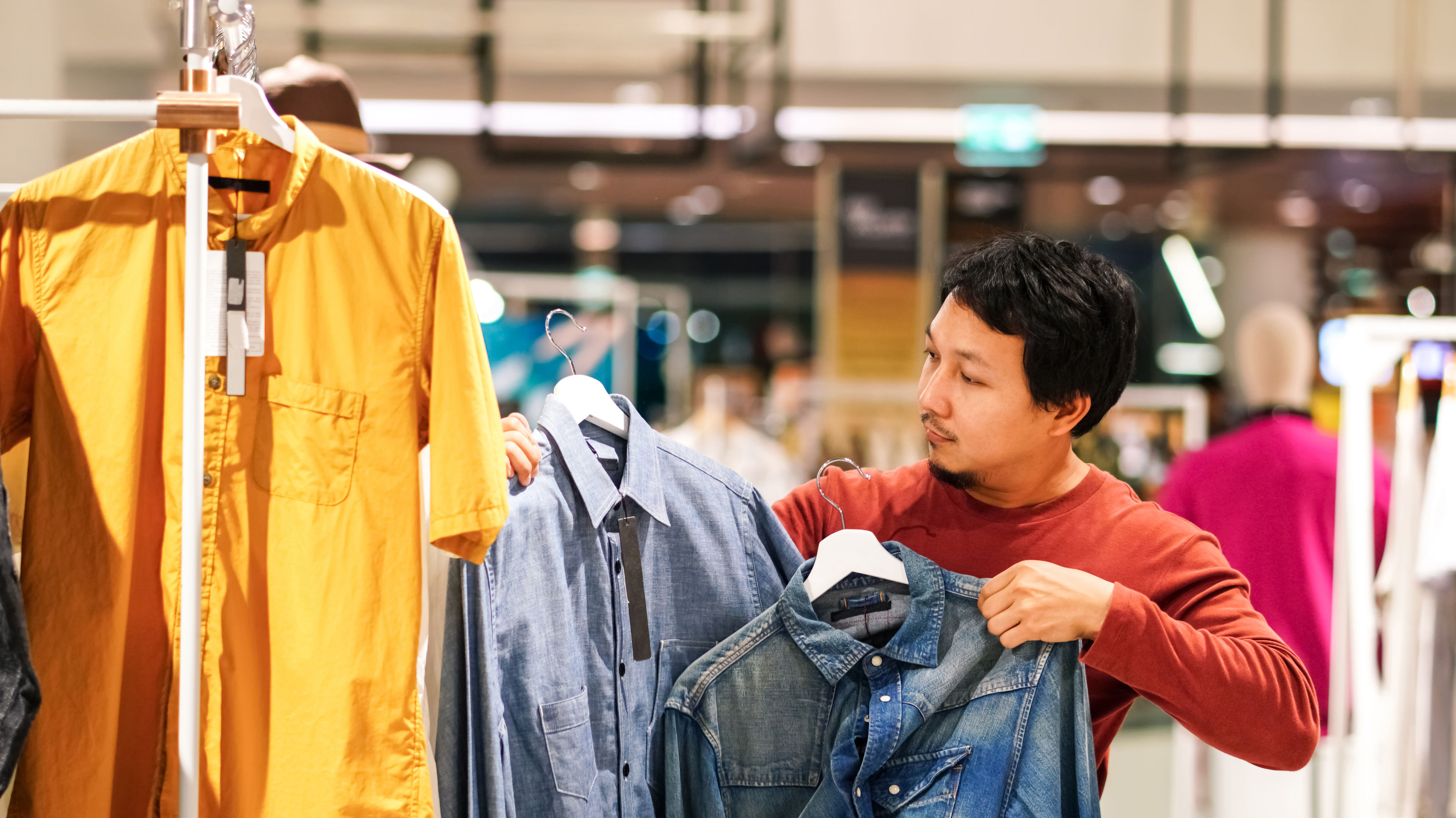 Smart man with beard choosing clothes in clothing store at shopping center.
