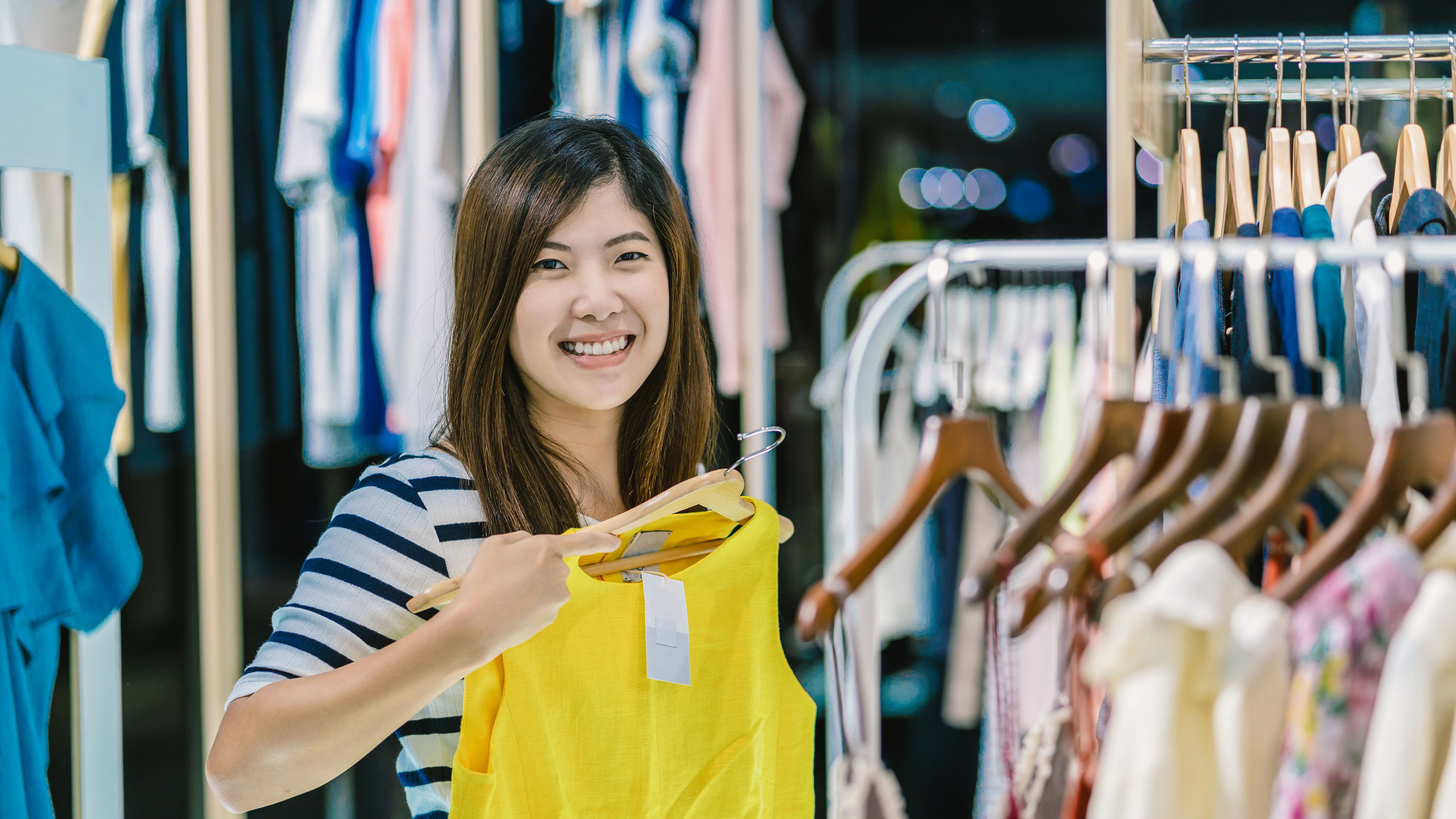 A smiling woman is shopping in a clothing store.