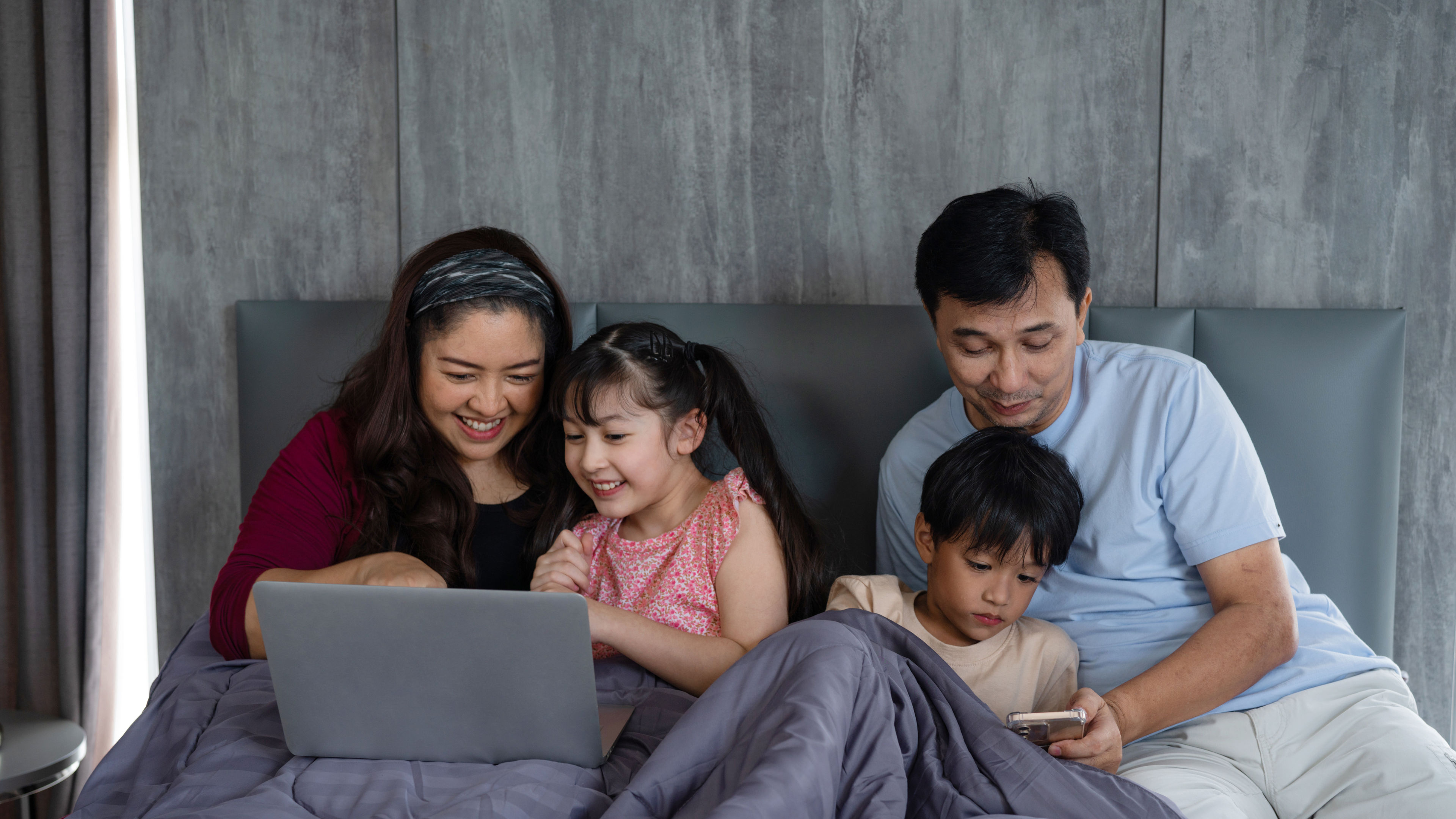 Parents with their children watching movies using laptop and smartphone.