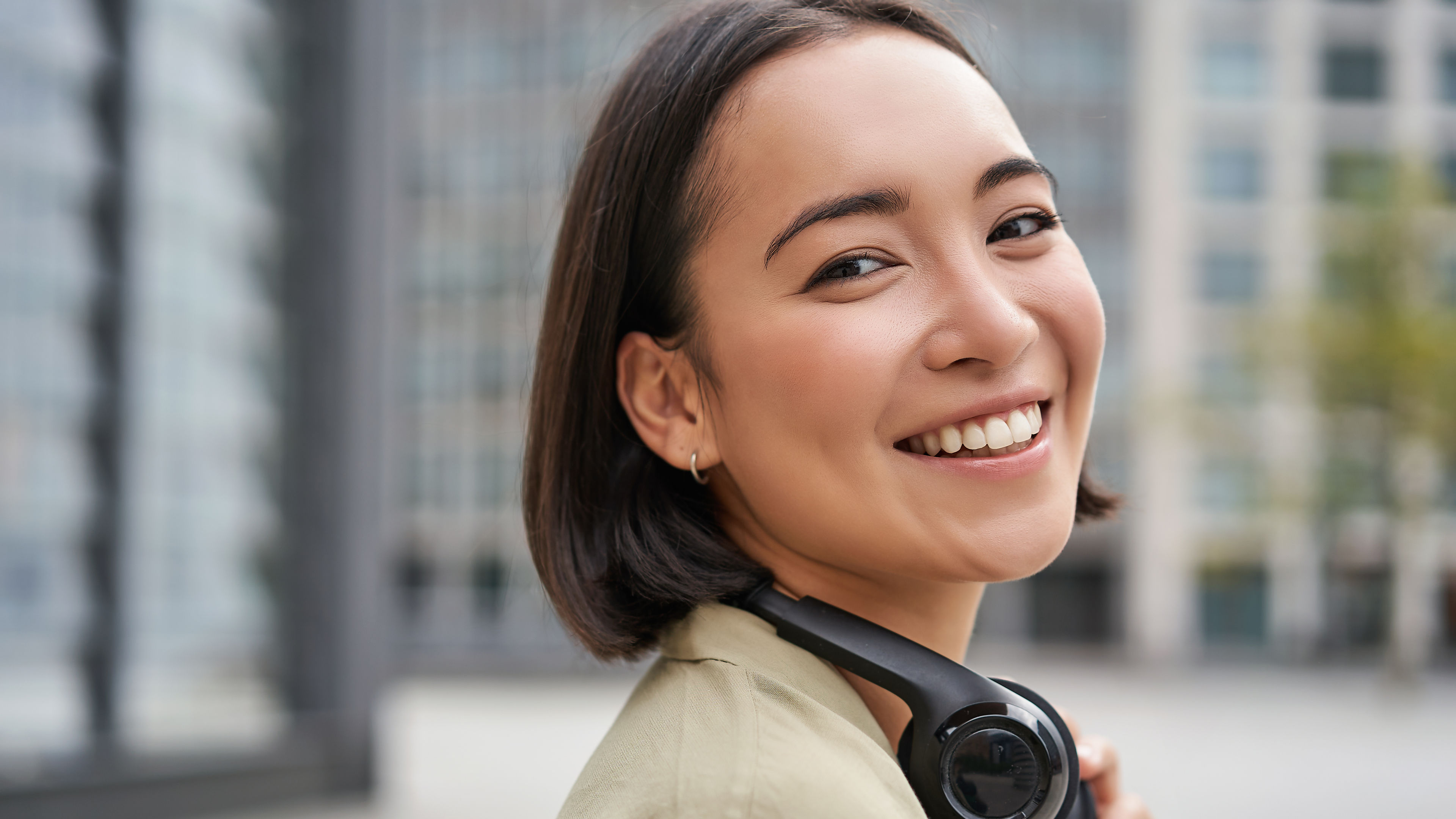 Portrait of a happy Asian woman in headphones enjoying music while walking in the city, smiling and laughing. 