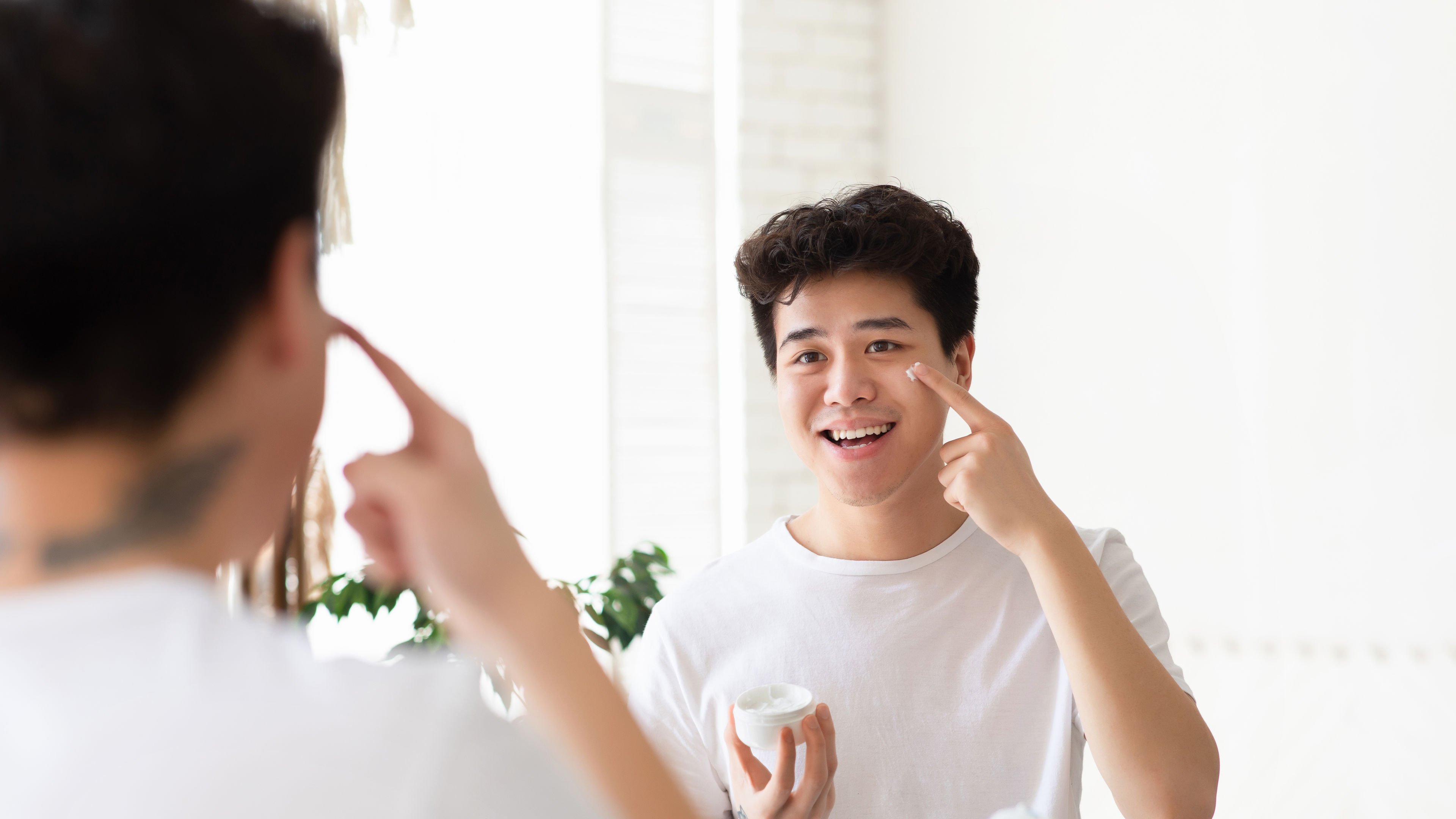 Man doing skincare and grooming in front of a mirror 