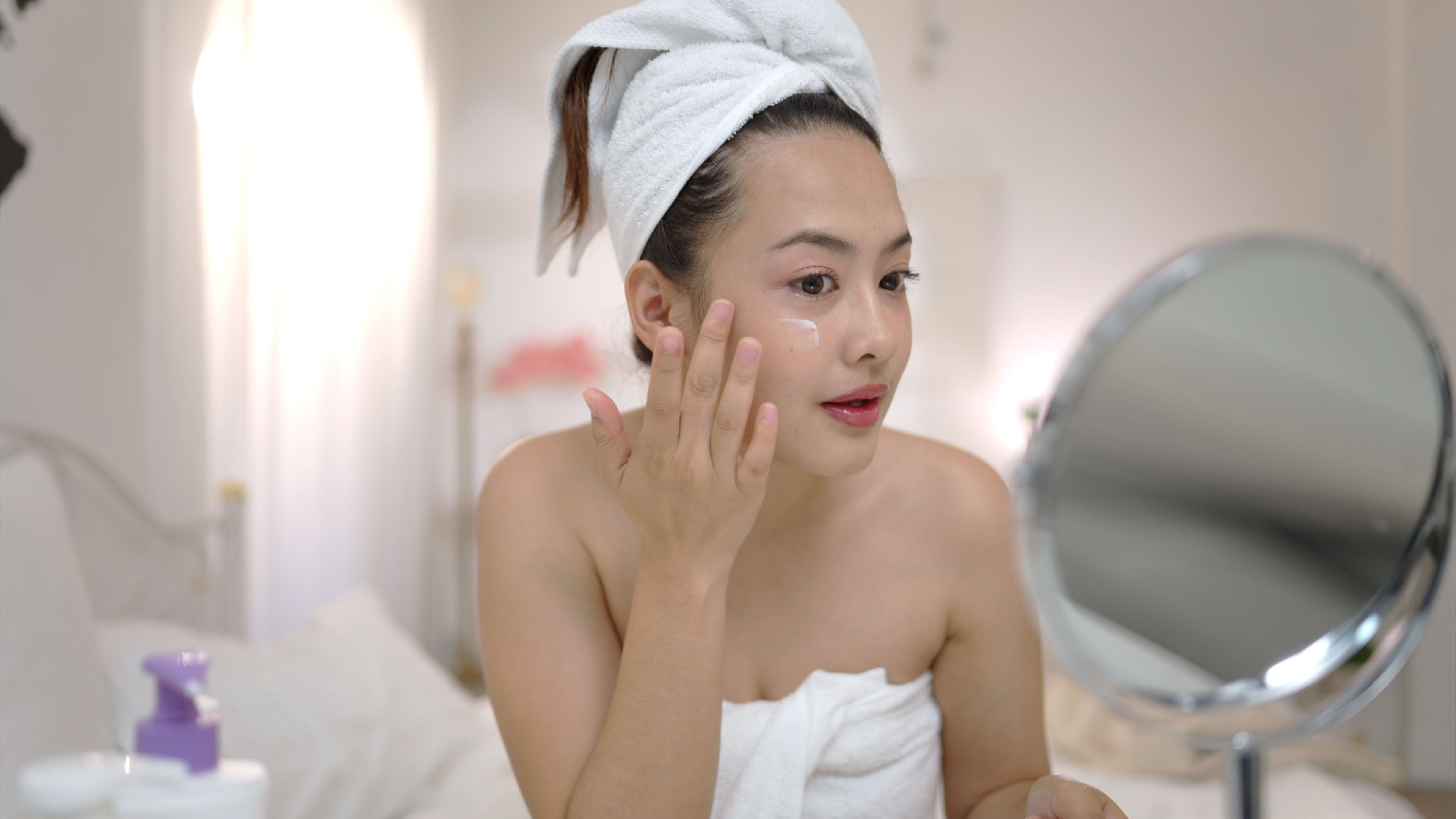 Pretty lady applying skincare dressed in a towel 