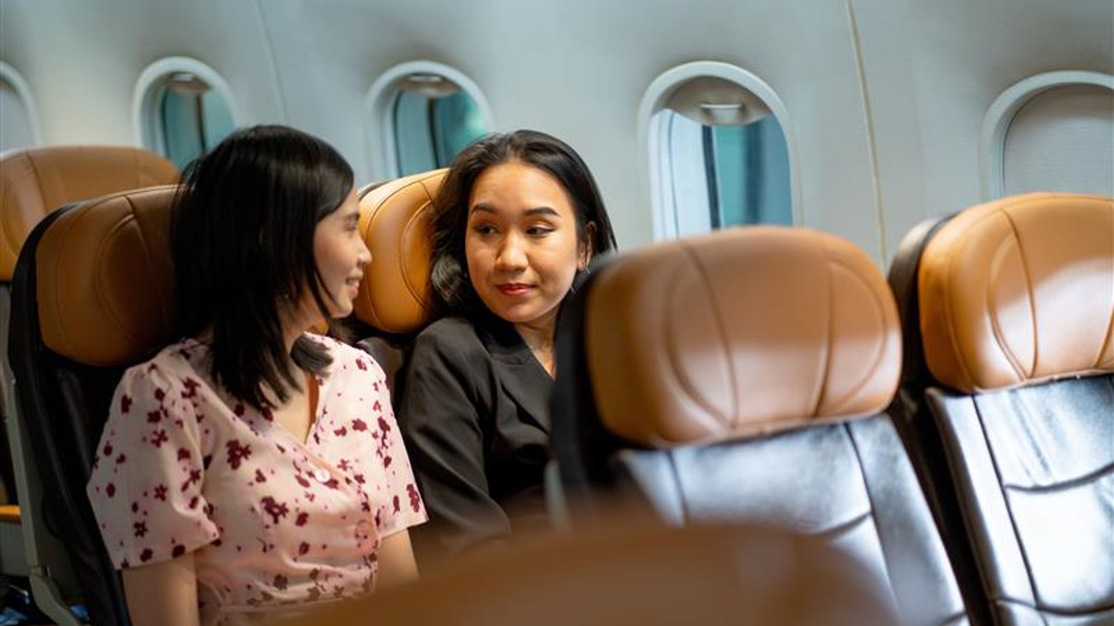 Two Asian passenger look like friends talk together in airplane during wait to take off and go to travel or work in other city.