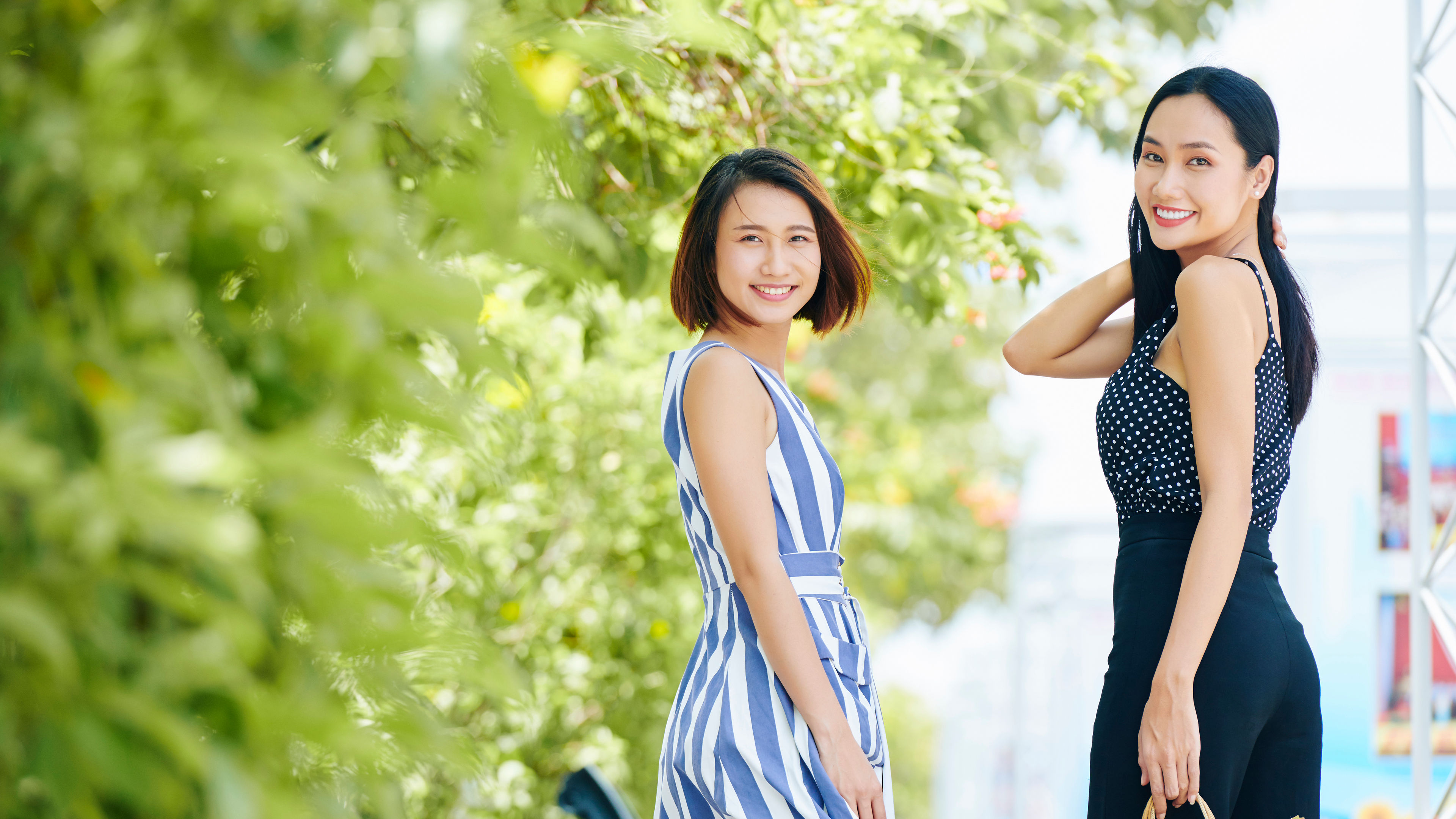Two Asian women are enjoying a joyful moment outdoors, possibly walking or chatting. 