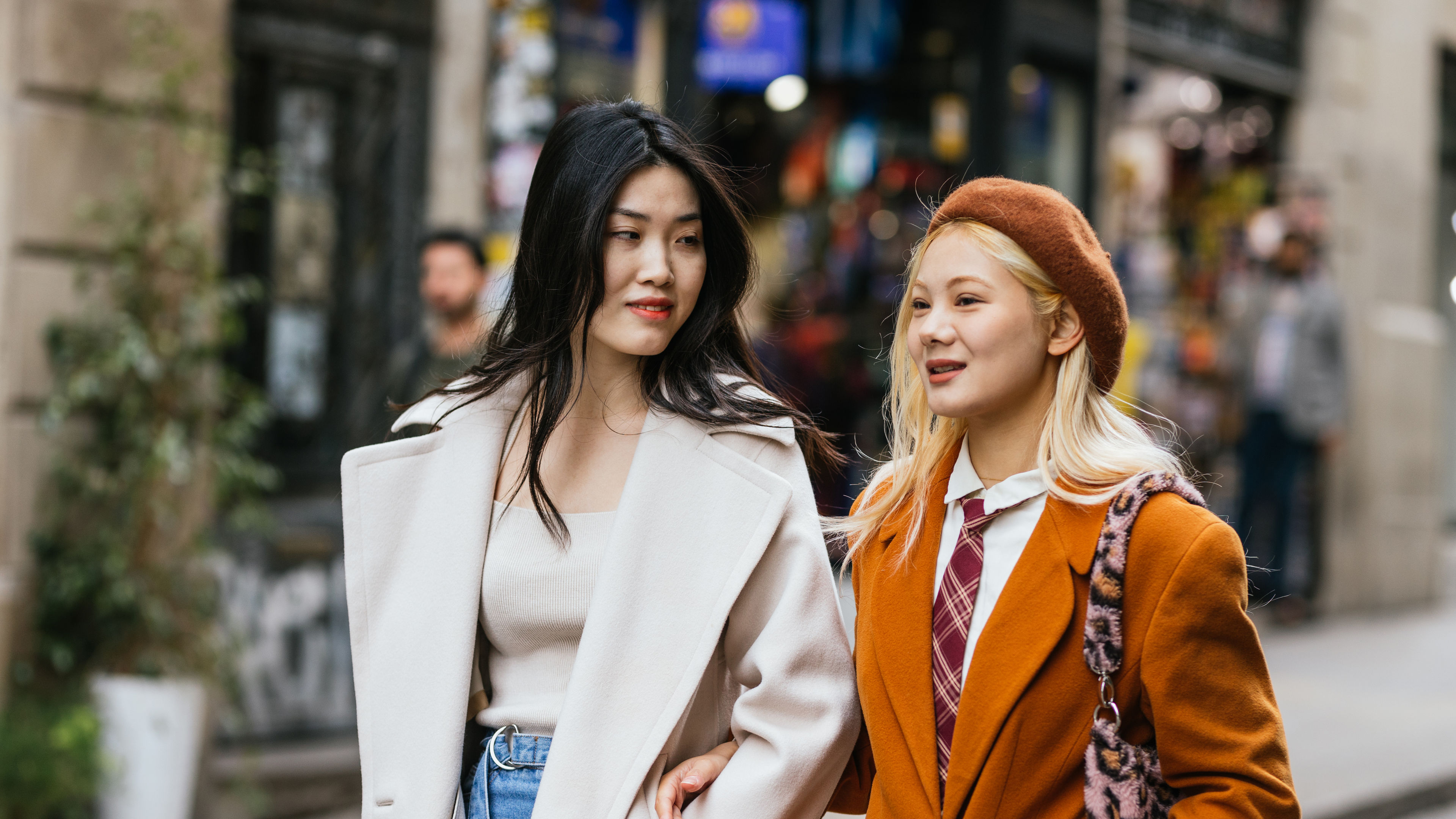 Two stylish young women arm in arm while walking on the street together.