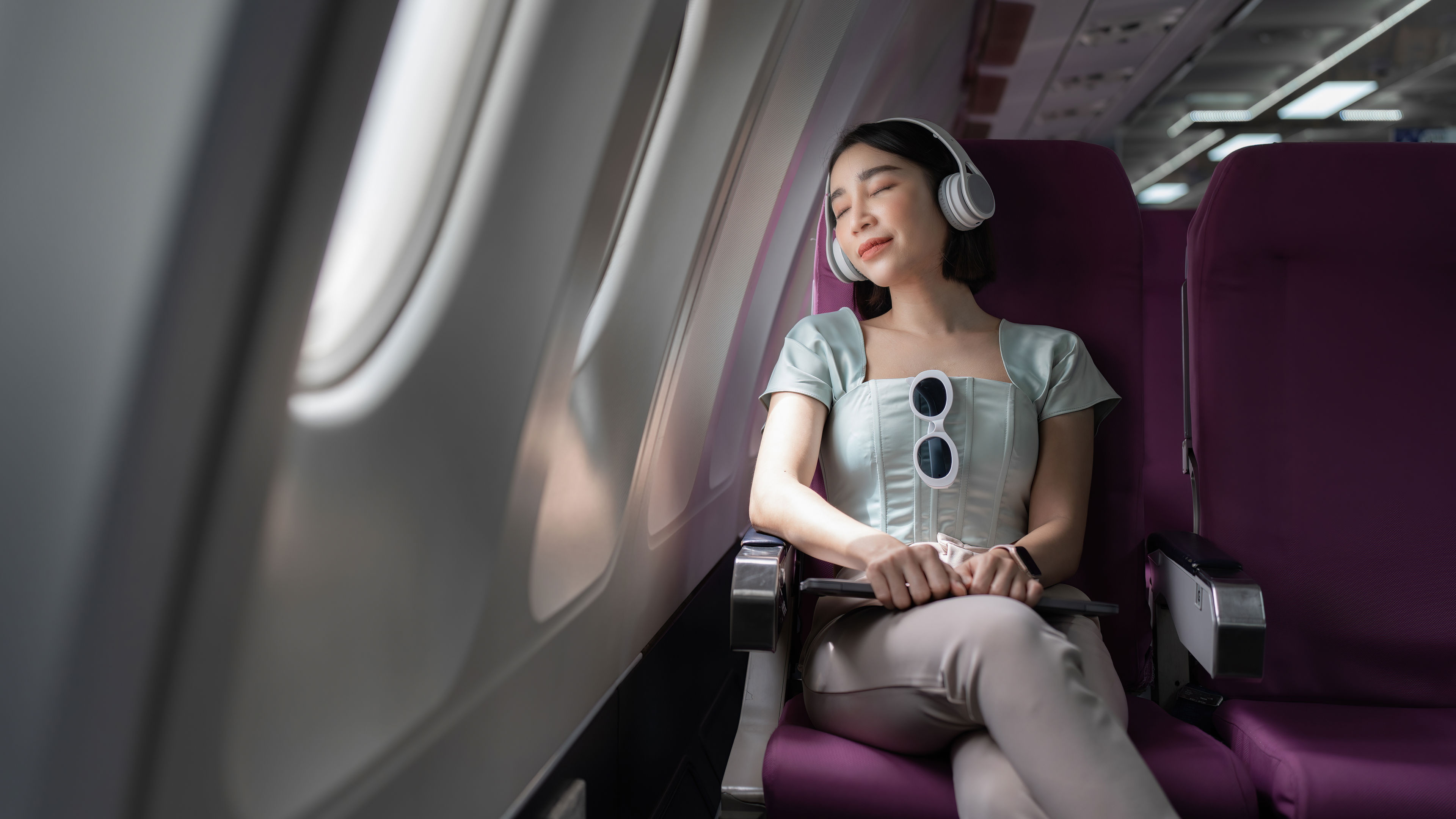 Joyful woman sits in the airplane and listen music while go to travel 